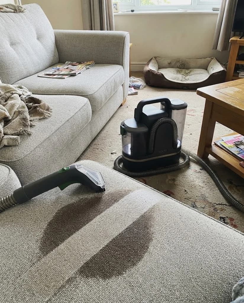 The Vekto Spot Cleaner P30 dirty tank held up to the light, full of brown water, a clean sofa arm behind it