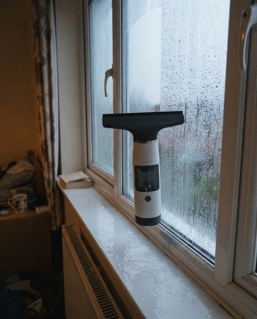 The Vekto Window Vac W10 held upside down along the bottom edge of a uPVC window, the sill dry beneath it